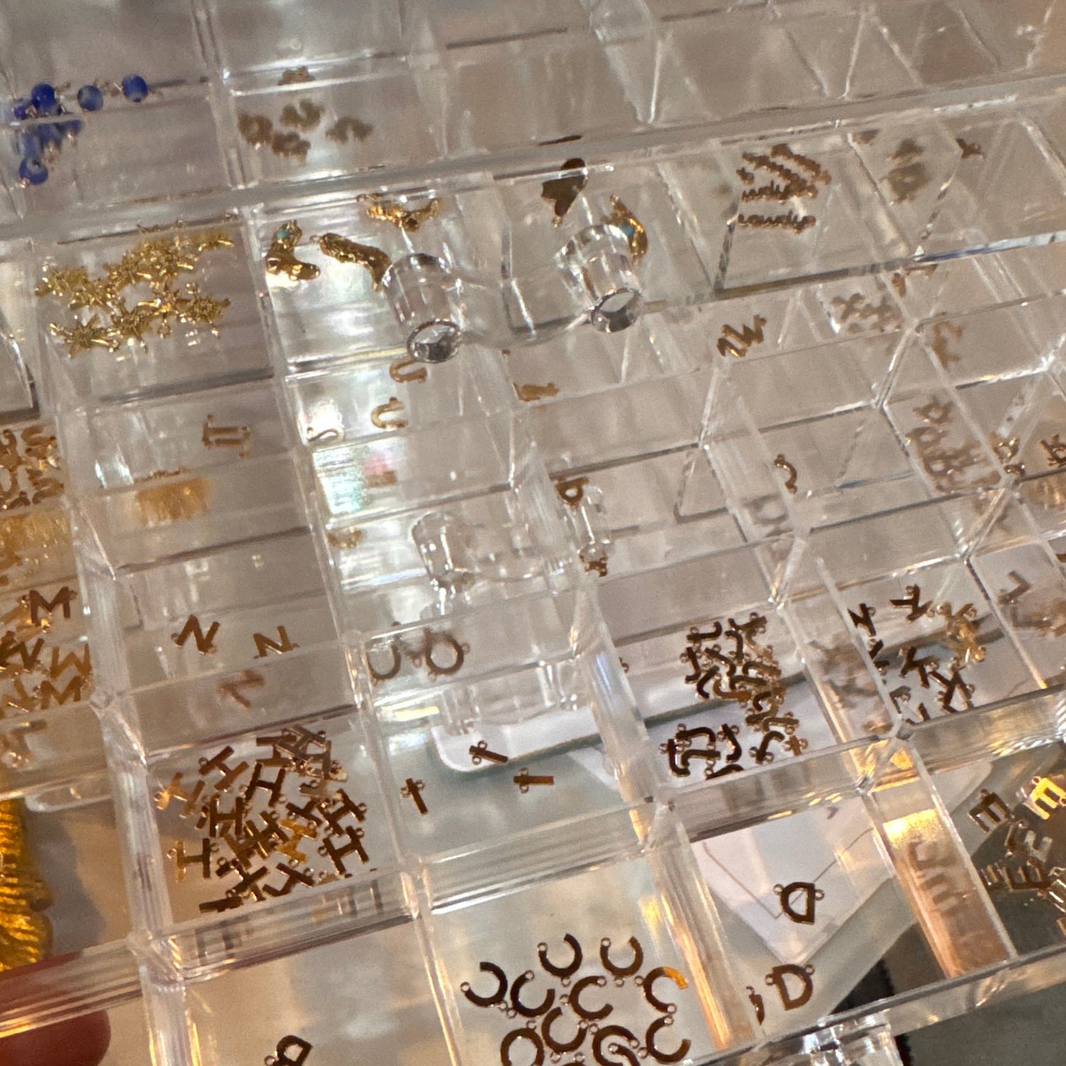 Picture of a plastic organization tray with a variety of different gold-filled charms for permanent jewelry.